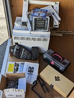 Window air conditioning unit with brackets, toolbox, tool belt, wooden box router bit set, and edge guide on floor.