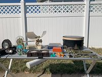 Wide shot of all items on white bench outdoors, showing the hat box, infant scale, clock, various brass items, and coin collecting kit.