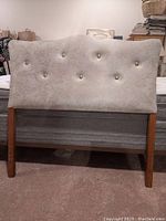 Front view of one padded vintage twin headboard showing light fabric with button tufting and wood legs.