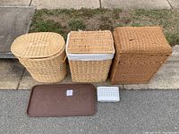Front view of three wicker hampers lined up with brown shoe tray and white bath caddy basket in front on sidewalk.