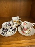 Three floral antique tea cups and matching saucers displayed on wooden shelf
