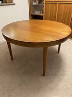 Full view of round teak dining table showing shape and tapered legs