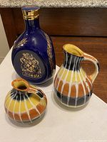 Haig Dimple cobalt blue glass decanter next to two East German pottery vases with striped pattern in yellow, orange, black and white
