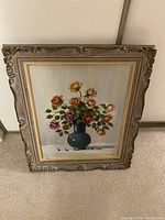 Front view of framed painting showing a vase with assorted colorful roses and an ornate carved wooden frame.