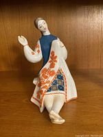 Front view of the ceramic figurine showing the lady sitting and waving with detailed orange and blue traditional dress patterns.