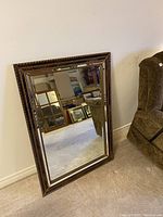 Full view of the large rectangular mirror leaning against a wall near a brown upholstered chair.