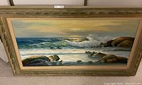 Front view of large framed seascape painting showing ocean waves and rocky shore under a glowing sky.