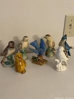 Seven decorative bird figurines arranged in a row on a surface against a wall, showing various colors and postures.