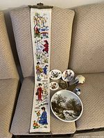 Long view of tapestry bell pull draped over a chair with six ceramic decorative items grouped beside it, showing the full lot arrangement.