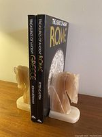 Photo showing the pair of onyx horse head bookends holding two hardcover books titled 'Treasures of Ancient Greece' and 'Treasures of Ancient Rome'. The horse heads and bases are polished onyx with natural striations.