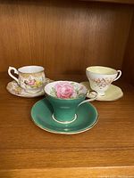 Photo of all three tea cups with matching saucers: Foley floral, light yellow floral, and green rose floral cup and saucers.