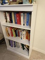 White bookshelf filled with multiple rows of assorted books including encyclopedias and fiction.