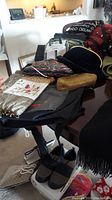 Photo showing assorted handbags and purses including a black floral glitter handbag, black velvet, gold woven clutch, white floral embroidered gloves, and a large black and gray handbag or tote on a table.