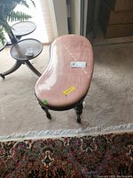 Vanity bench showing kidney-shaped pink upholstered seat and carved wooden legs, viewed from above angle.