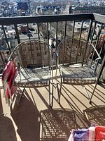 Two metal patio chairs with woven seat and backrest and one red folding beach chair on a balcony.
