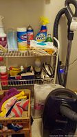 Photo showing Kenmore vacuum, cleaning bottles including OxiClean and Clorox, aerosol can, white iron, and assorted cleaning cloths on shelving.