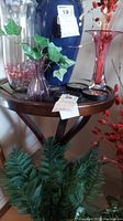 Full view of round wooden side table with mirror top and four figurine coasters on top surrounded by decorative vases and floral arrangements.
