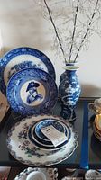 Photo of the five decorative plates stacked and blue and white floral vase displayed on a glass shelf.