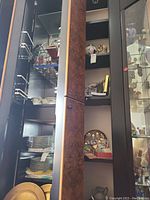 Tall black cabinet with glass doors containing stacked plates, bowls, decorative jars, and smaller collectibles.