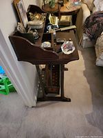 Side angle view of dark wooden vintage desk with raised back edge and various items on the surface, showing leg design and scratches on desk surface.