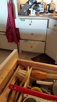 Photo showing wooden knife block holding knives on kitchen counter with toaster oven and coffee maker in background, and two drawers partially open showing cooking utensils.