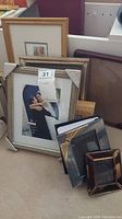 Multiple assorted picture frames of varying sizes, colors and materials arranged leaning against a wall with a photo book.