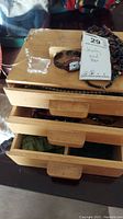 Wooden jewelry box with three drawers open showing jewelry inside; visible wear on box, scratches and scuffs on surface.