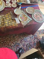 Five Asian motif pillow covers including two larger embroidered ones, two decorative plates, and an Asian soup bowl with spoon on a burgundy tablecloth