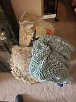 Four linens including Wanamaker's crochet bedspread, knit blanket, crochet cover, and needlework swatch visible, placed on carpet.
