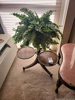 Wooden plant stand with faux fern floral from a side and top angle showing two round wood surfaces and dense faux leaves.