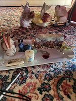 Top-down photo showing majority of the rabbit figurines including cloisonne, crystal, ceramic, heart necklace, Peter Rabbit candle, and soap bar on a white ceramic tray.