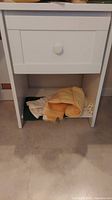 Photo of the full white wood shelf showing drawer and lower shelf with cloths.