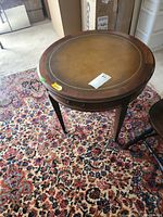 Full top view of round side table with leather surface on patterned rug.