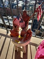 Overview of the clay statues arranged on the round table with American flags, showing multiple handmade statuettes in reddish-brown clay.