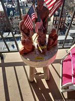 Side table with five sculpted figures and American flags on top, outdoor balcony setting, showing table and figures front view.