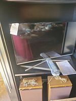 Photo of Samsung 33-inch Series 5 LED TV with silver stand, placed on a shelf with remote and user manual.
