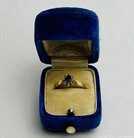 Open blue velvet ring box displaying front view of ring with cluster setting
