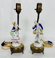 View of the pair of porcelain lamps featuring colonial couple figurines mounted on ornate metal bases with electrical fittings.