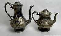 Photo showing the full set of the coffee pot and tea pot, highlighting their shape and engraved decorations.