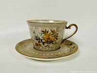 Front angle view of tea cup on saucer showing floral and dotted design with gold handle