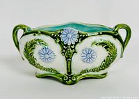Front view showing rectangular planter with two handles, green leafy scrolls and blue flowers on white background, turquoise interior.