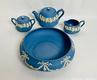 Photo of full Ecanada jasperware style blue tea set with teapot, sugar bowl, creamer, and serving bowl grouped together showing white relief decoration.