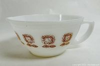 Side view of milk glass batter bowl with brown sunflower pattern, handle, and pouring spout visible