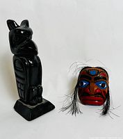 Front view showing the black bird totem and the front of the painted mask with attached hair strands.