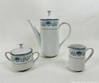 Photo showing the full tea set: teapot, sugar bowl, and creamer with blue floral pattern and gold trim on white porcelain.