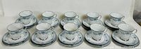 10 blue and white Noritake tea cups with matching saucers and plates arranged in rows on a white surface