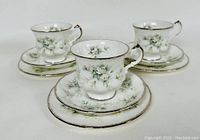 Three sets of tea cups, saucers, and dessert plates showing floral pattern and silver trim