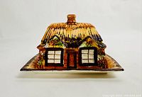 Front view of the cottage-shaped ceramic butter/cheese dish with detailed hand-painted roof and windows.
