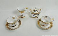 Tea set display with cups, saucers, creamer, and sugar bowl showing gold floral details and 50th anniversary markings.