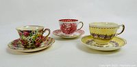 Three decorative tea cups and matching saucers displayed side by side on white background.